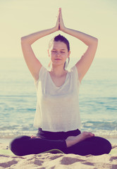 Fototapeta na wymiar Sportswoman in white T-shirt is sitting and practicing yoga
