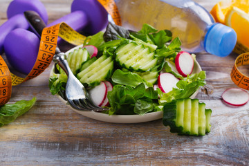 Healthy vegetarian salad, dumbbells and bottle of water on wooden table
