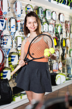 Female standing in sporting goods store with balls and racket