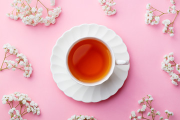 Cup of tea with fresh flowers on pink background. Top view. Copy space