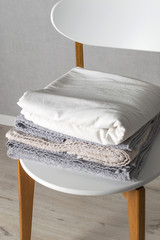 Fototapeta na wymiar Monochrome colors. Stack of home linen on the chair in scandinavian style. Domestic cleaning