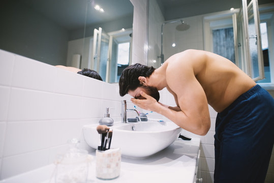 Attractive Man Washing His Face In The Bathroom Sink Getting Ready For Work.