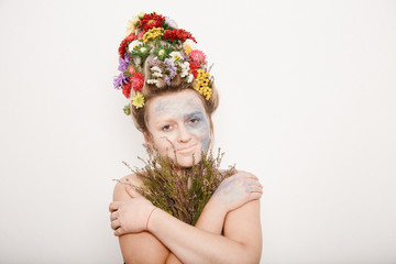 A young woman with flowers on her head and hands. Spring image with flowers. Man with a colorful plant. The girl and the blooming haircuts and brocade on her face.