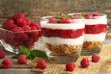 Dessert with raspberries and granola in glasses on grey wooden table