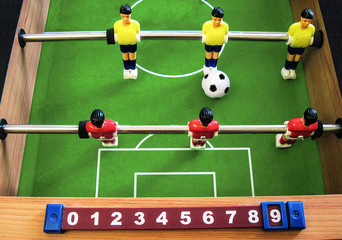 Table football soccer with a scoreboard. Yellow and red players on a vivid green field with a big ball. Two metal rods and wooden sides. Table game for sport and recreations for kids and adults