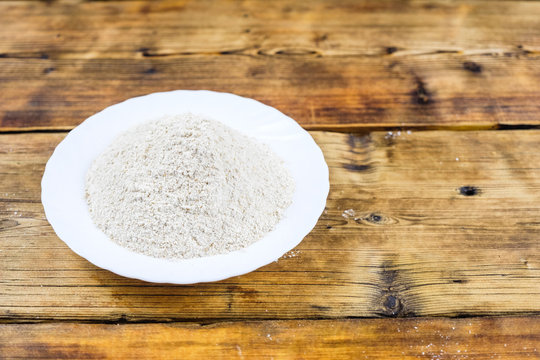 Close-up heap with wheat flour coarse in white plate on wooden background. Left on the photo.