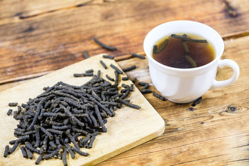 Close-up fermented Ivan-tea on wooden board Dry herbal natural tea White cup with Ivan-tea