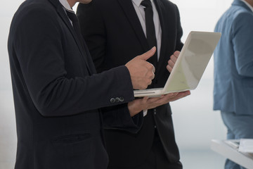 Business man standing and showing trumps up to his colleague after discussion about the work topic shown in laptop.