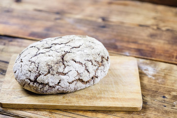 Homemade fresh rye bread on board on wooden background. Left on photo.