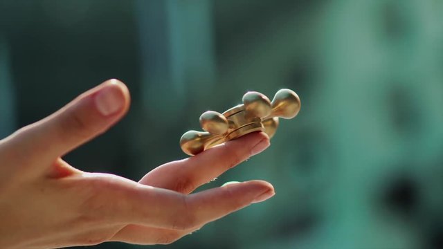 Close up shot of female's hand keeping golden fidget spinnet in her hand. Spinner slowly rolling on her finger.