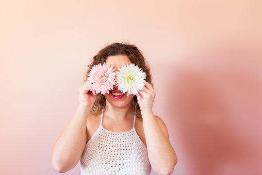 Beautiful curly woman holding two flowers, pink and white on color background at home. Hello Spring concept.