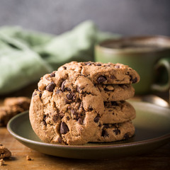 Chocolate chip cookies on green plate with cup of coffee on old wooden table. Selective focus.