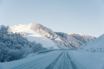 Snow road and car tracks on the road in the winter in the North Caucasus. Snow-covered trees and mountains. The concept of winter travel by car