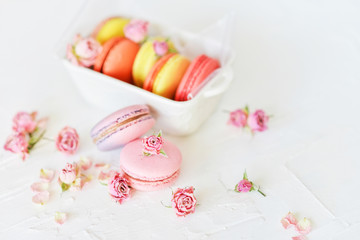 Fototapeta na wymiar Dessert: A Delicate Fresh French Macaroons In Pastel Colors Gift Box With Flowers Roses On A Light Textile Background