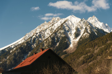 Red roof of a house on a background of a mountain with a snow-capped summit. The concept of a dwelling in the mountains. Holidays in the mountains
