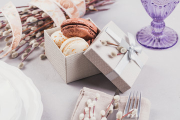 White plate, purple glass, cutlery, present box with macaroons and pussy willow twigs