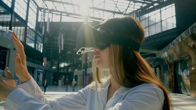 a young woman with virtual reality glasses on her head is standing in a shopping center, a lady is using a smartphone and a special presentation on a gadget