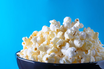 Popcorn on blue background in black shiny bowl