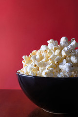 Popcorn on a red background in a black shiny bowl