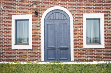 The facade of the house with a blue arched door and square windows on the sides