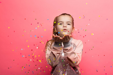 Happy girl celebrating on a pink background. Blows up multicolored confetti