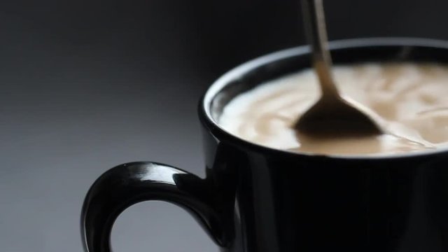 Close up shoot with black cup of coffee. Stir the cappuccino with a silver spoon