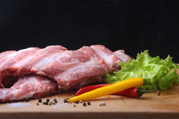 Raw Ribs on a rustic cutting board with salt, pepper and grinder for spices . Black Background for copy space. Top View.
