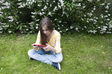 Naklejka na ściany i meble Beautiful teenager girl with tablet computer sits on the grass in Park. Photo