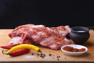 Raw Ribs on a rustic cutting board with salt, pepper and grinder for spices . Black Background for copy space. Top View.