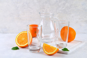 Clean empty glasses and a jug with orange slices on a light background.