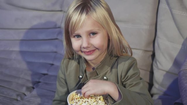 Cute little girl eating popcorn smiling to the camera at the cinema