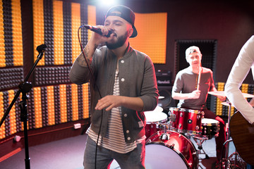 Portrait of modern hip-hop singer performing with his band in recording studio while making new...