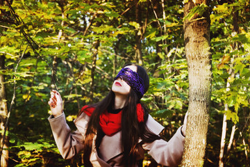 A girl with blindfold looks up into the sky in the forest