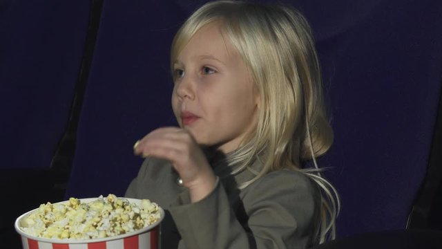 Close up of an adorable little girl eating popcorn while at the movie theatre