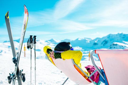 Picture from back of woman in armchair, skis, sticks in snowy resort