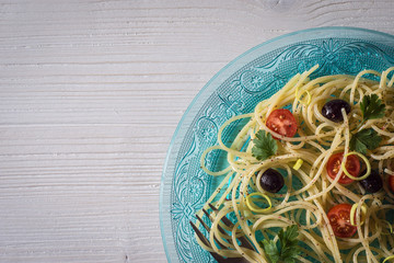 Teller Spaghetti mit Tomaten, Oliven und frischen Kräutern auf weißer Holztisch