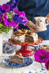 A woman and a cake of thin pancakes with white cream and nuts. Milkman with flowers in the hands of the girl. Spring fresh flowers. Breakfast in the morning. Card.