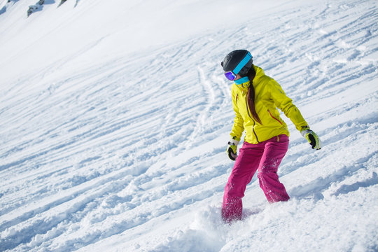 Image of brunette athlete wearing helmet and mask, snowboarding from snowy mountain slope