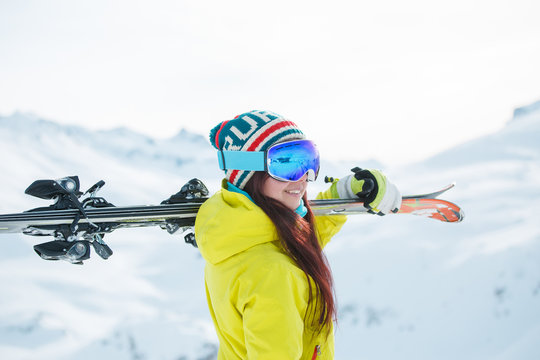 Side view of smiling woman in mask with skis on her shoulder