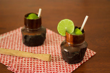 Rustic wood glass with Caipirinha the most famous brazilian cocktail. In the wood table with  red checkered napkin. Lemon slices - Brazilian National Drink 