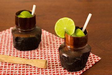 Rustic wood glass with Caipirinha the most famous brazilian cocktail. In the wood table with  red checkered napkin. Lemon slices - Brazilian National Drink 