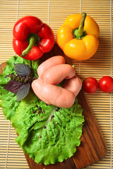 Sausages with cheese on a wooden board with lettuce, basil, cherry tomatoes and paprika.