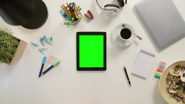 A finger scrolling on a tablet with a green screen. The tablet is on the white table. View from the top. Close-up.