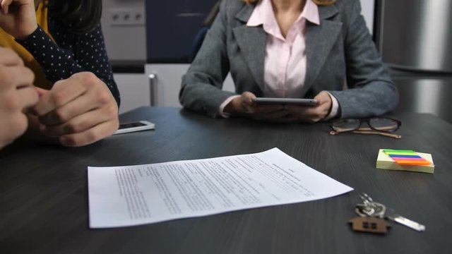 Midsection of realtor and family couple sitting at table. Husband's hands reading house purchase agreement, putting signature and shaking hands with agent. Family signing mortgage contract. Dolly shot