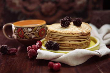 pancakes with frozen berries pile in a green plate with a cup of milk on a dark wooden table 