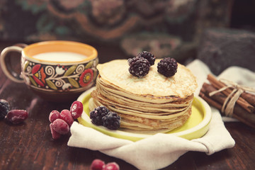 pancakes with frozen berries pile in a green plate with a cup of milk on a dark wooden table 