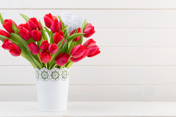 Fresh red tulip flowers bouquet on shelf in front of wooden wall.