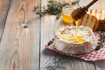 Fototapeta na wymiar A real Camembert from France with thyme, honey and toasted bread on old wooden rustic table. Soft cheese on a wooden background with copy space