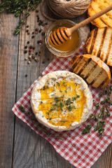 A real Camembert from France with thyme, honey and toasted bread on old wooden rustic table. Soft cheese on a wooden background. Top view