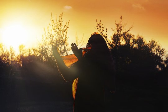 Praying time . Silhouette of young woman praying to god .Light from sky .eclipse . to hold a scarf in hand . decline sky . silhouette against the sun . ray of light .
